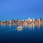 An image of the downtown Seattle skyline from Puget Sound. The sky and the water are very blue.