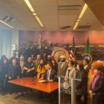 Mayor Harrell signing executive order at a big desk with a group standing around him at City Hall.